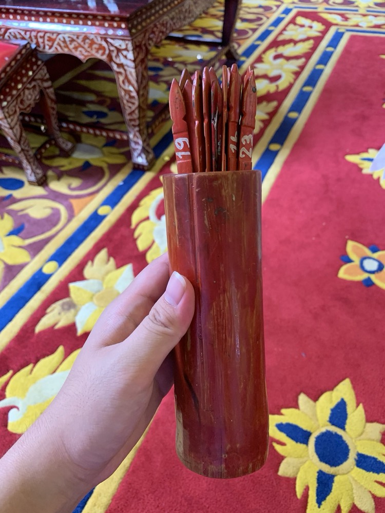 มือถือกระบอกเซียมซีไม้ไผ่ที่มีไม้ติ้วเขียนตัวเลขอยู่ภายใน ในศาลาวัด